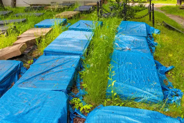 Parlak mavi su geçirmez örtüler huzurlu bahçedeki bahar bakım sezonunda mezarlıkları koruyor.