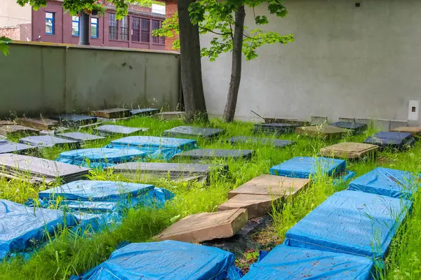 Mavi koruyucu örtüler ve bakım malzemelerinin bulunduğu mezarlık yolu devam eden koruma çabalarını ve bakımını gösteriyor.