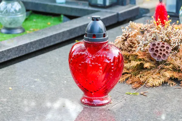 Mezarlığın mezar taşına çam kozalağı süslemeli kırmızı kalp şeklinde anıt mum.