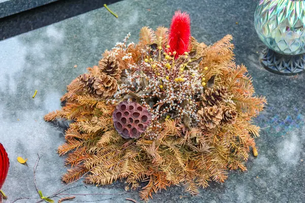 Çam kozalağı süslemeli geleneksel kurumuş çiçek hatıra çelengi yıpranmış beton yüzeye yerleştirilmiş.