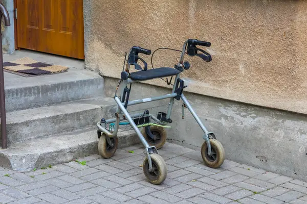 Gri beton basamaklara yerleştirilmiş, tekerlekleri olan gümüş renkli bir çerçeve kapı aralığına çıkıyor, yardım ve ulaşılabilirlik öneriyor..