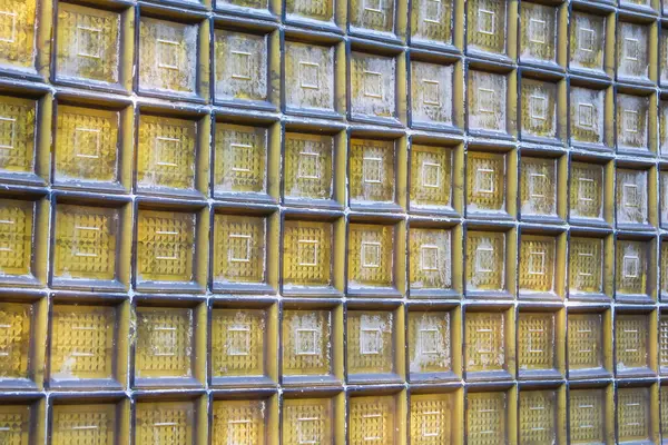 Şeffaf cam blok bir duvar yakın çekim ızgara deseni ile, soyut bir arkaplan dokusu oluşturur sıcak, altın renkli.