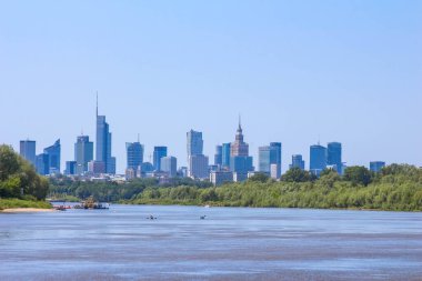 Modern şehir binaları ve gökdelenler sakin göl boyunca doğal kıyı şeridi altında parlak mavi gökyüzü altında görüldü.