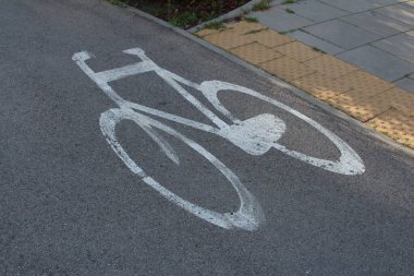 Koyu asfalt yol yüzeyine çizilmiş beyaz bisiklet sembolü bisiklet şeridini ve kentsel ulaşım altyapısını gösteriyor