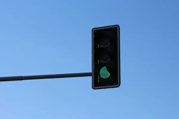 Açık mavi gökyüzüne karşı yeşil trafik ışığı sinyali ve şehir ulaşım altyapısını gösteriyor
