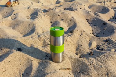 Kumlu sahilde tek başına duran yeşil kamp feneri atmosferik akşam havası yaratıyor.