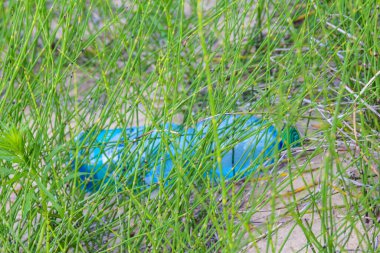 Uzun yeşil çimenlere yakalanmış parlak mavi plastik poşet çevre kirliliği karşıtlığı yaratıyor