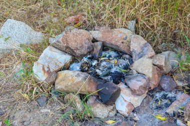 Kömürleşmiş kalıntılarla çevrili taş kamp ateşi halkası dışarıda kamp alanı oluşturuyor.
