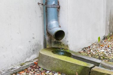 Çakıl taşı yüzeyine akan su ile metal drenaj borusu kentsel altyapı detaylarını oluşturuyor