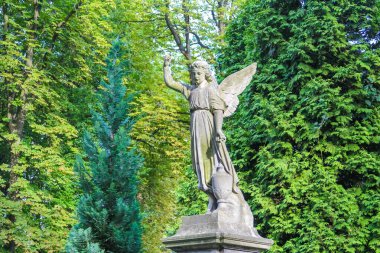 Etrafı yeşilliklerle çevrili, huzurlu bahçeye uzanmış kanatları olan melek heykeli.