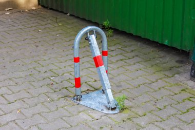 Kırmızı ve beyaz çizgili beyaz metal park engeli kaldırıma monte edilmiş.