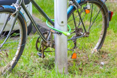 Şehir ortamında zincir güvenlik sistemiyle metal direğe kilitlenmiş yeşil bisiklet.