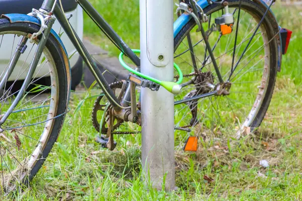 Şehir ortamında zincir güvenlik sistemiyle metal direğe kilitlenmiş yeşil bisiklet.