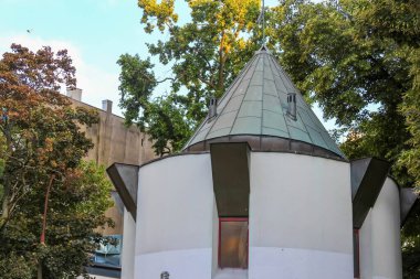 Yeşil konik çatılı beyaz silindirik kule huzurlu park ortamında sonbahar ağaçlarının arasına yerleşmiş.