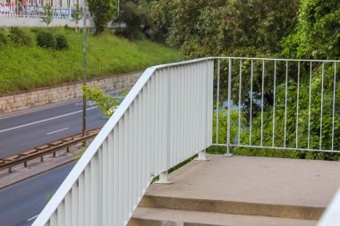 Dikey parmaklıkları olan modern metal korkuluklar ağaçlarla çevrili peyzaj alanı ve yeşil alanı koruyordu.