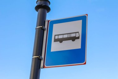 Metal direğe asılmış mavi belediye otobüs durağı tabelası parlak gökyüzüne karşı açık toplu taşıma bilgilerini gösterir