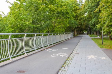 Metal parmaklıkları ve yemyeşil ağaçları olan modern yaya geçidi huzurlu bir şehir geçidi oluşturuyor.