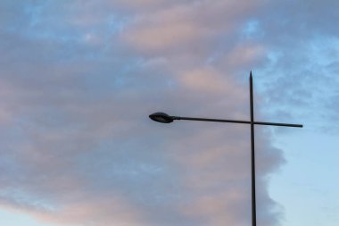 Alacakaranlıkta dramatik bulutlu gökyüzüne karşı modern sokak lambası silueti kentsel atmosfer yaratır