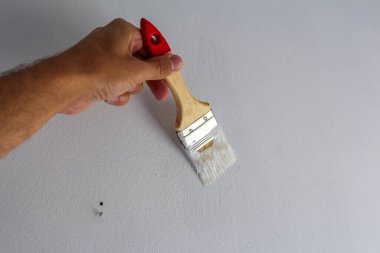 İnsan eli, resim dersi için beyaz yüzeye karşı kırmızı saplı düzgün boya fırçası tekniğini gösteriyor.