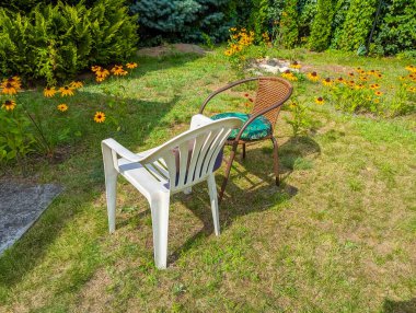 Açık havada güneşli bir teras yakınında yeşil çimlere yerleştirilmiş beyaz plastik bahçe sandalyesi.