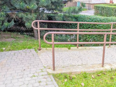 Yeşil peyzaj alanının yakınına beton yüzeye kurulmuş metal korkuluk sistemi güvenli ve erişilebilirlik sağlıyor