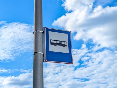 Parlak bulutlu arka planda metal direğe monte edilmiş mavi otobüs durağı tabelası