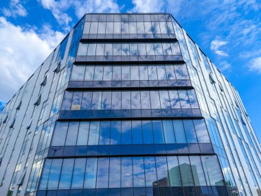 Modern glass office building photographed from ground level showing reflective blue sky in facade windows