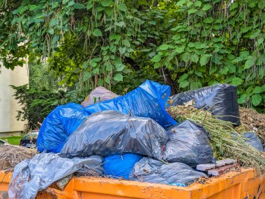 Yeşil bitki ve çalılara saçılmış çok sayıda siyah çöp torbası.