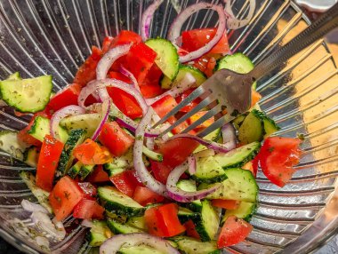 Kırmızı biberli taze sebze salatası ve ahşap yüzeydeki cam kasede servis edilen yeşiller sağlıklı yemek sunumunu oluşturur.