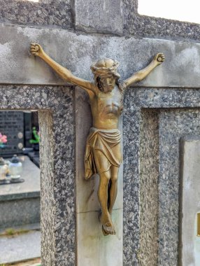 Golden crucifix mounted on stone cemetery cross monument displaying religious symbol of faith and eternal life in memorial setting