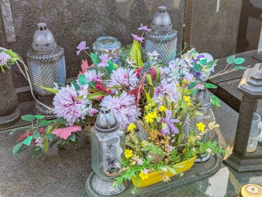 Artificial flower arrangements with various seasonal blooms positioned in cemetery planters creating colorful memorial garden display for tribute purposes