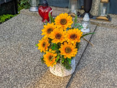 Bright yellow sunflowers arranged in white vase placed on cemetery stone pathway creating cheerful memorial flower tribute