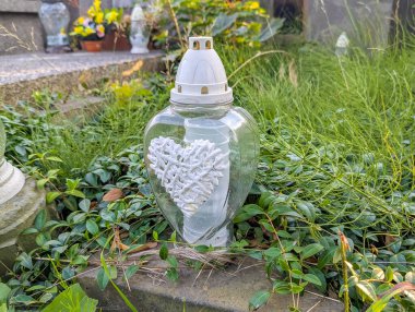 White memorial lamp with decorative elements positioned among green grass and vegetation creating peaceful cemetery lighting tribute