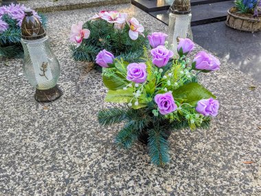 Mor çiçekler ve anıt mumlar yıpranmış mezar taşında dokunaklı bir haraç düzenlemesi oluşturur.