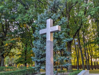 White memorial cross standing solemnly among green trees in peaceful cemetery or memorial park setting