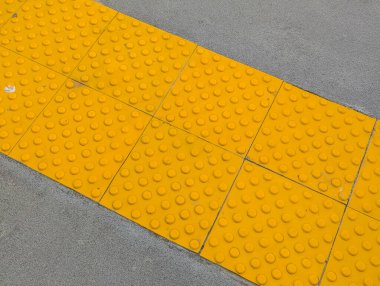Beton zeminde görme engelli erişimi için yükseltilmiş noktalar desenli parlak sarı dokunsal yüzey