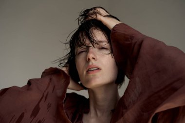 Burgundy kapüşonlu, dağınık saçlı ve derin düşüncelere dalmış bir gencin yakın plan portresi.