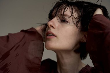 Islak saçlı, bordo giysili ve derin düşüncelere dalmış genç bir portre.