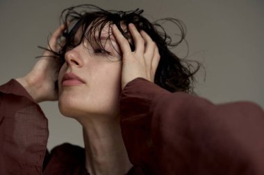 Saçları ıslak ve elleri saçlarında duygusal hassasiyet ve orijinallik gösteren genç biri.