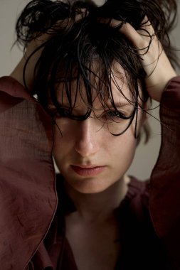 Islak saçlı bir gencin portresi. Hafif ışıklandırmalı, bordo bir elbiseyle aşağıya bakıyor.