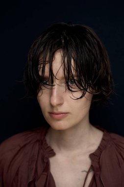 Burgonya rengi saçı olan genç adam koyu renk arka planda ve karamsar ışıklandırmayla dalgalandı.