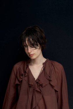 Burgundy kapüşonlu genç kadın stüdyo ışıklandırmasında kendine güvenen pozuyla ayakta duruyor.