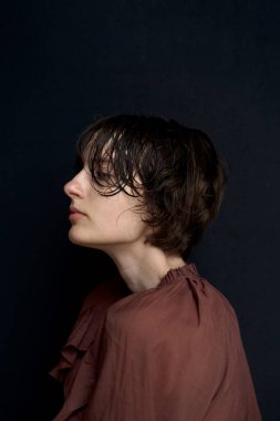 Burgundy bluzlu genç bir kadın stüdyo ışıklarında rüya gibi bir ifadeyle yukarı bakıyor.