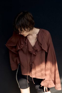 Burgundy gömlekli genç bir kadın yumuşak doğal ışıklandırmayla aşağı bakarken yakasını düzeltiyor.