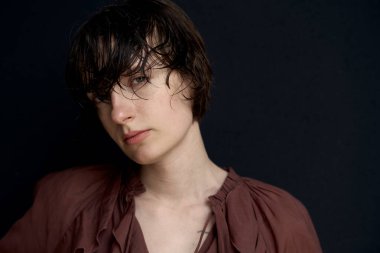 Burgundy bluzlu genç bir kadın kameraya özgüvenli ve sakin bir ifadeyle bakıyor.