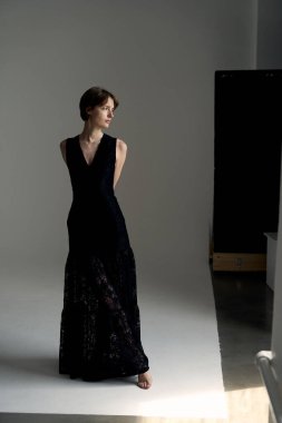 Çekici esmer manken çağdaş stüdyo fotoğrafçılığında dalgalı siyah gece elbisesi giyiyor.