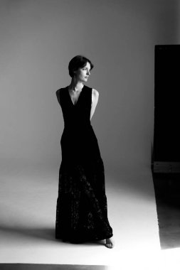 Gösterişli siyah cüppeli profesyonel model. Minimalist stüdyoda geometrik gölgeli zarif bir poz veriyor.