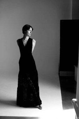 Mimari unsurlarla sanatsal stüdyo aydınlatmalarında yakalanmış dramatik siyah elbiseli şık bir kadın.