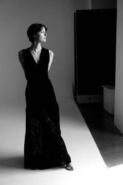 Zarif siyah elbiseli güzel bir kadın minimalist stüdyo ortamında özel tasarım elbise sergiliyor.