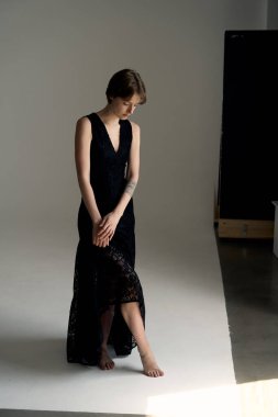 Çağdaş stüdyo fotoğrafçılığında uzun siyah elbiseli profesyonel model zarif bir şekilde yerde oturuyor.